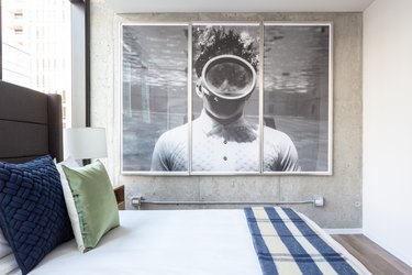 Industrial loft bedroom with large dark wood headboard, large black and white photo on wall, striped blanket.